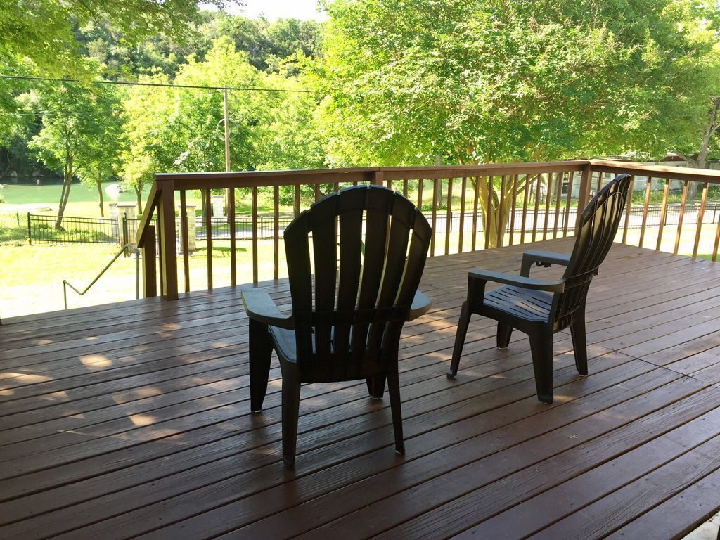 A wooden deck with two Adirondack chairs and a table, overlooking a lake and trees.