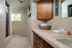 A bathroom with a bathtub, a wooden cabinet, a wicker basket with towels, and a window with a view of greenery.