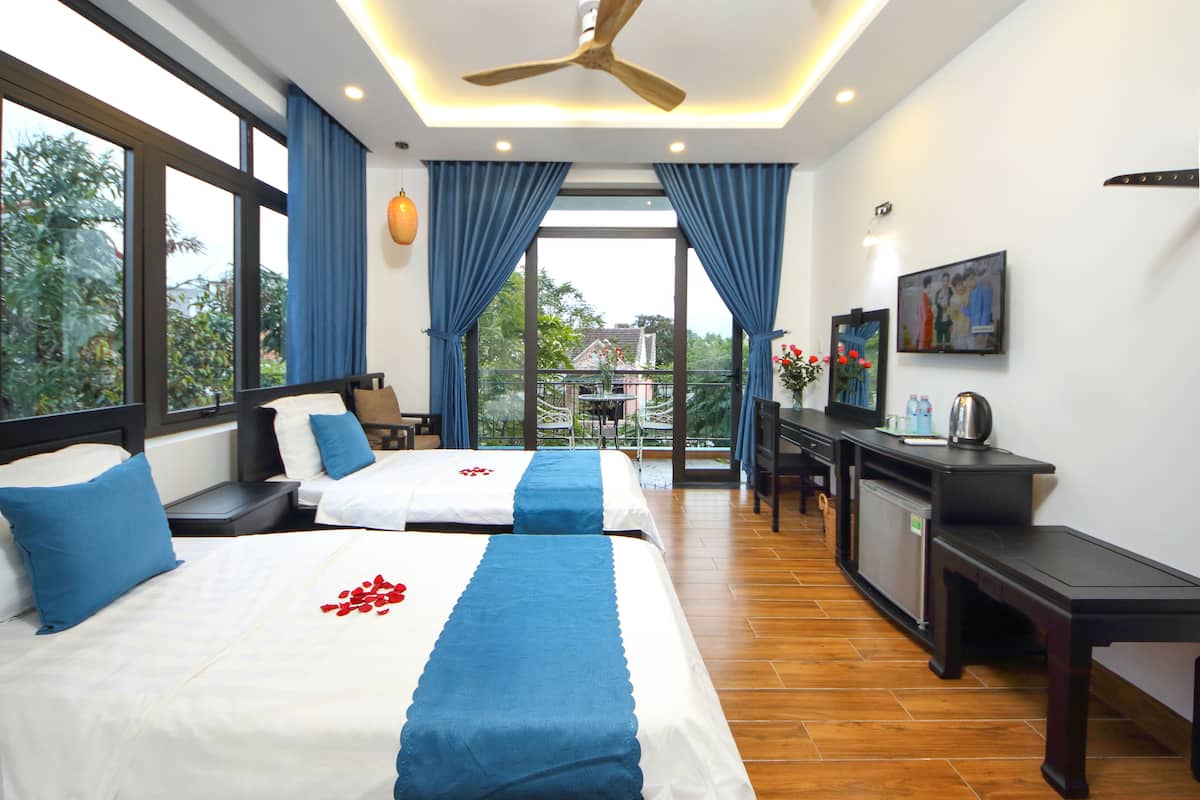 A hotel room with two beds, a desk, a chair, a TV, and a balcony with a view of the outside.