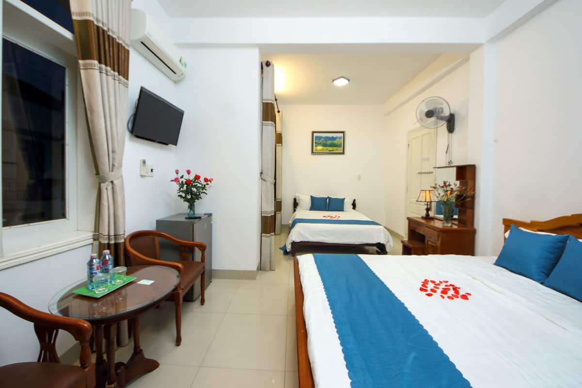 A hotel room with a bed, a desk with a chair, a TV mounted on the wall, and a window with curtains.