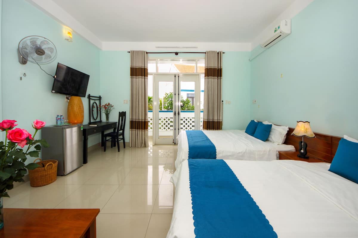 A hotel room with two beds, a desk, a chair, a TV, and a view of the outside.