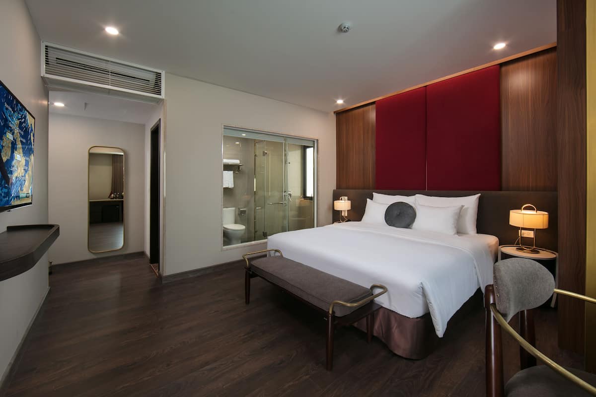 A modern hotel room with a large bed, bedside lamps, a bench, and a view of the bathroom.