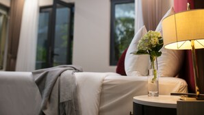 Ett hotellrum med en säng, ett nattduksbord med en lampa, en vas med blommor och ett fönster med gardiner.