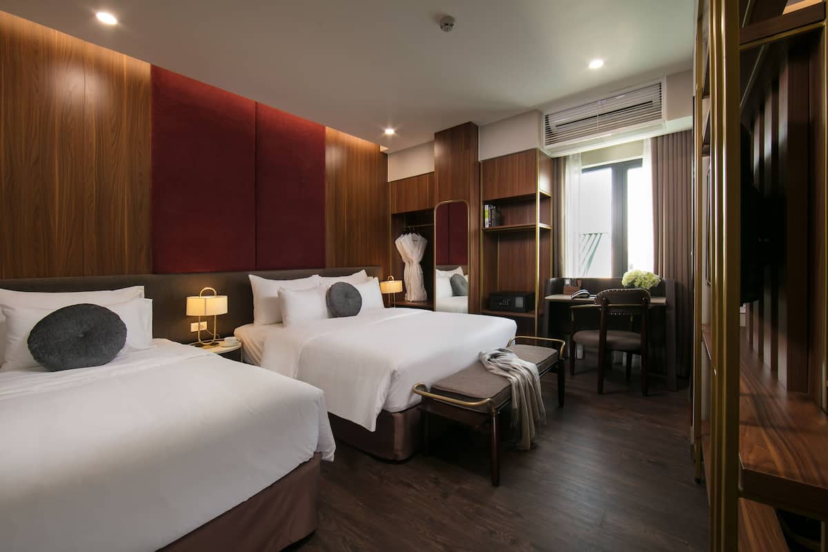 A hotel room with two beds, a desk, a chair, a small table, and a wardrobe.