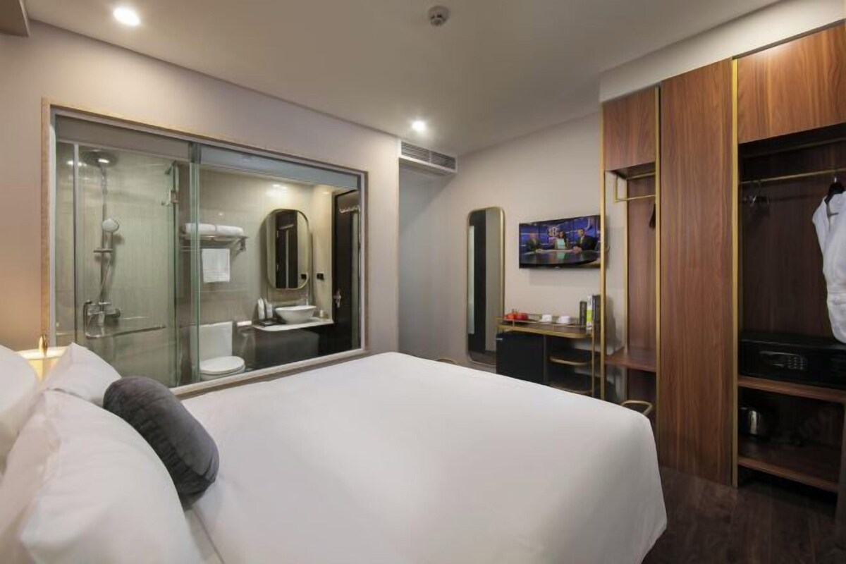 A hotel room with a large bed, a glass shower enclosure, a wooden wardrobe, and a television on the wall.