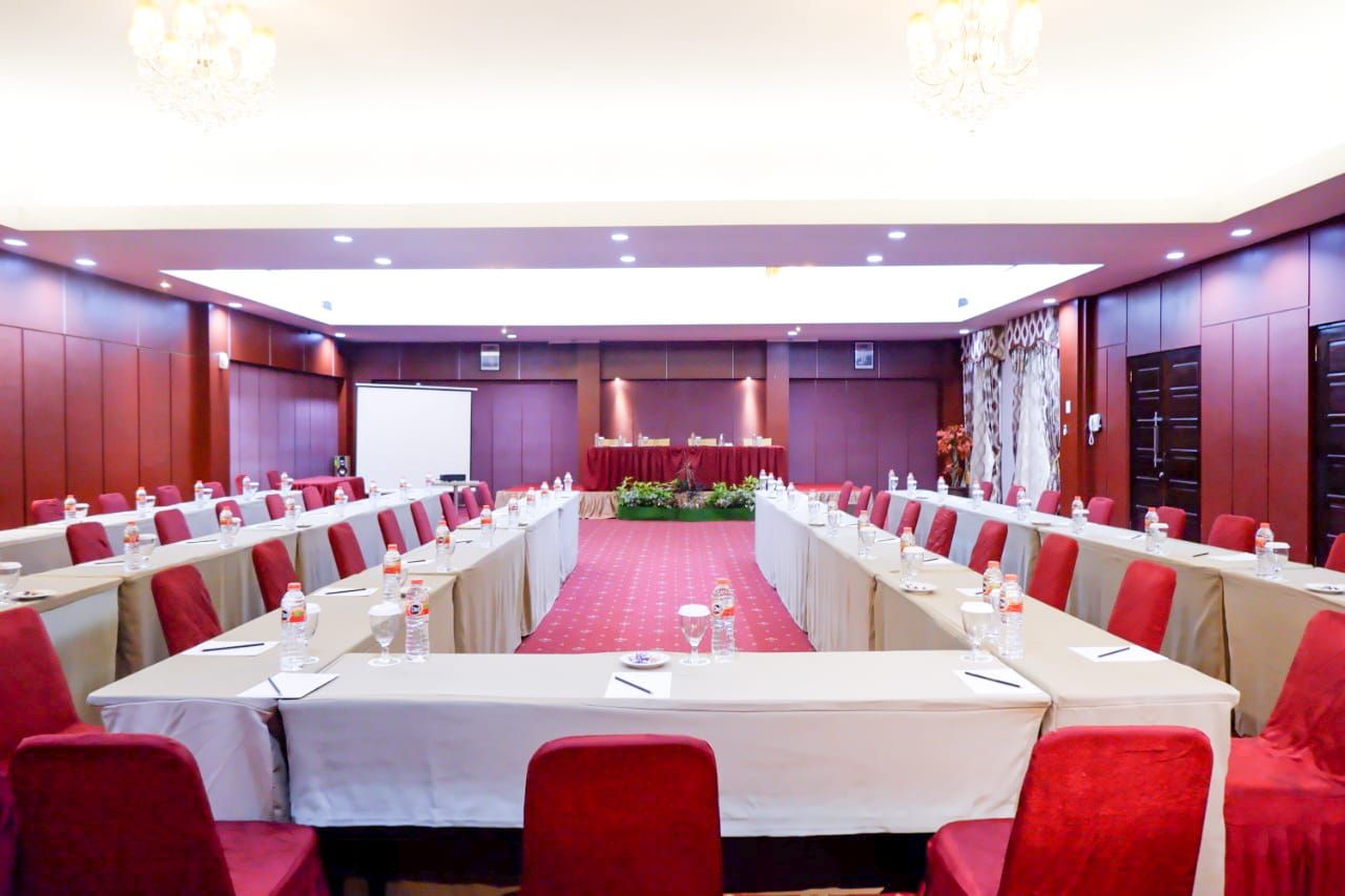 A conference room with a long table, red chairs, and a stage with a red carpet.