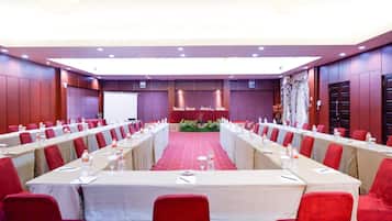 A conference room with a long table, red chairs, and a stage with a red carpet.