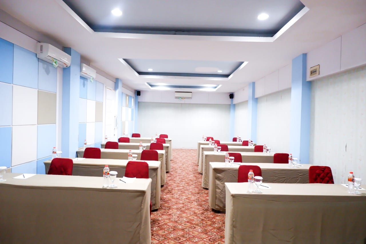 A conference room with rows of tables and chairs, air conditioning units, and a patterned carpet.