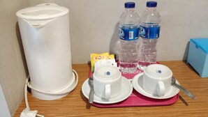 Una cafetera, dos botellas de agua, una caja de pañuelos y dos tazas con cucharas sobre una bandeja.