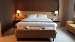Habitación de hotel con una cama grande, dos mesitas de noche con lámparas, un sofá pequeño y un otoman con toallas.