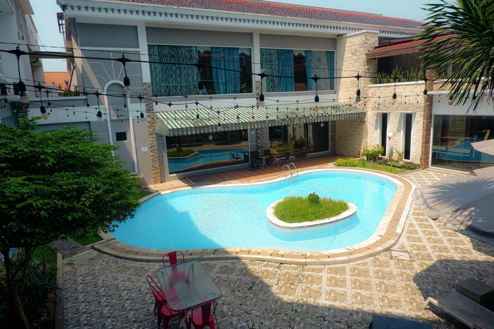 Une piscine entourée d’un patio, un espace salon couvert et une vue sur un immeuble doté de nombreuses fenêtres.