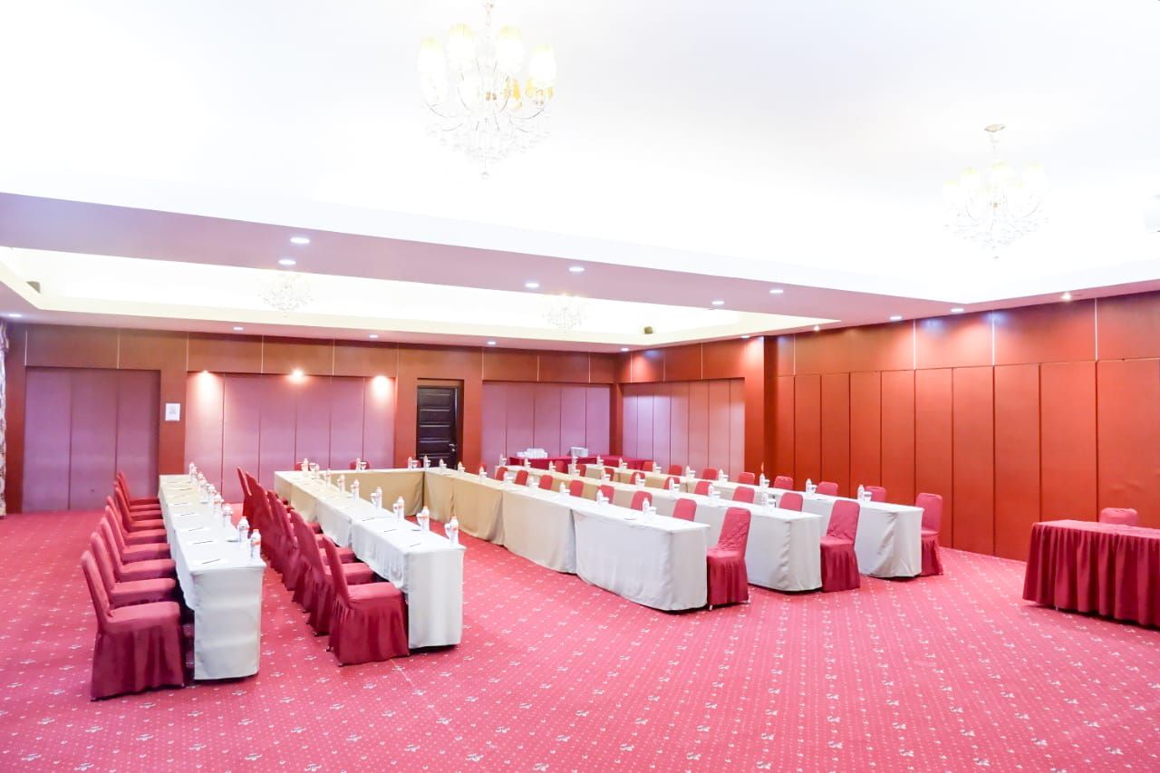 A conference room with long tables and chairs, a chandelier, and a red carpeted floor.