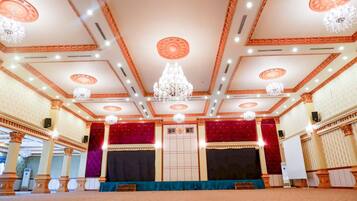 Un salón amplio con escenario, techo ricamente decorado y candelabros.