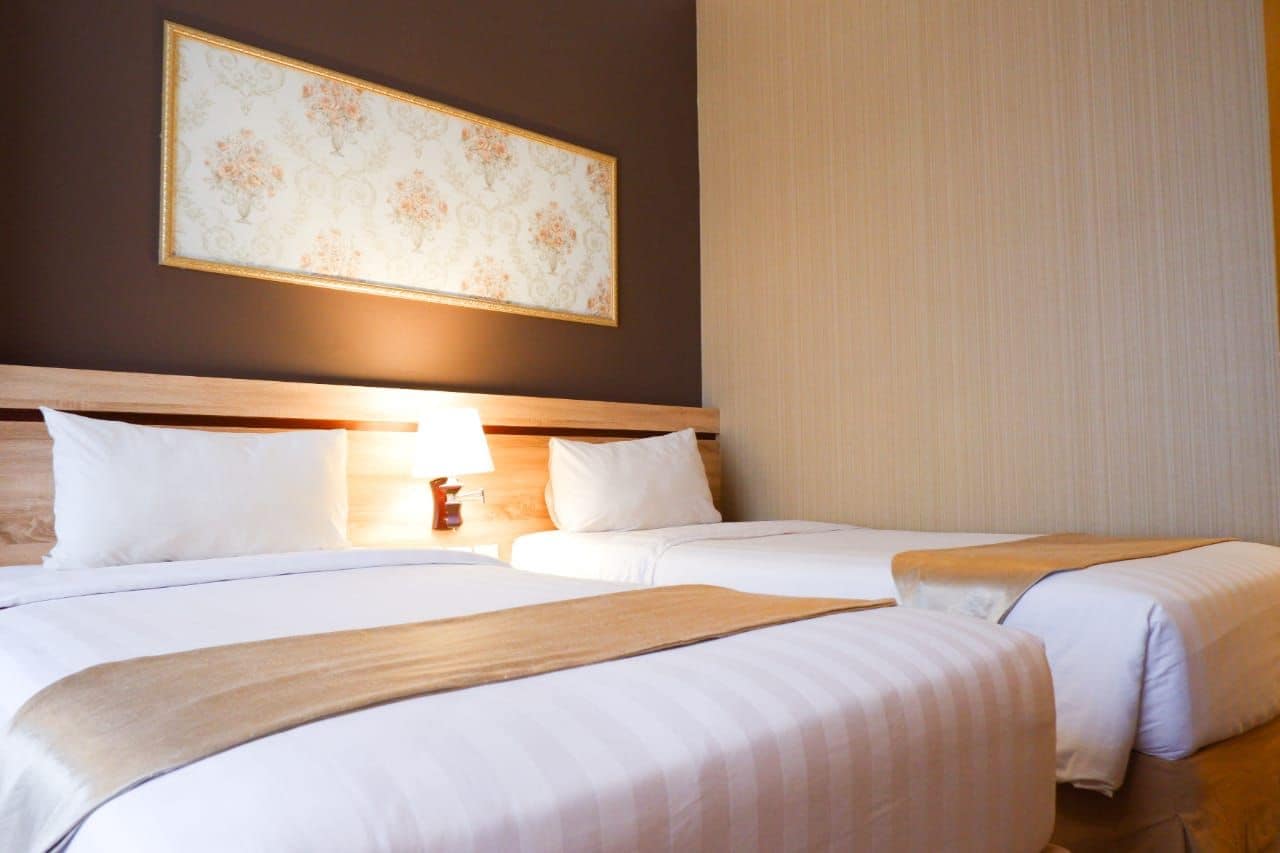 A hotel room with two beds, a nightstand with a lamp, and a large floral artwork on the wall.