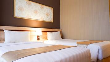 A hotel room with two beds, a nightstand with a lamp, and a large floral artwork on the wall.