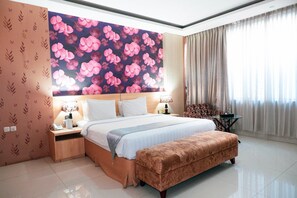 A hotel room with a large bed, bedside tables, a desk, and a patterned wall. - Horison Altama Pandeglang (Pandeglang)