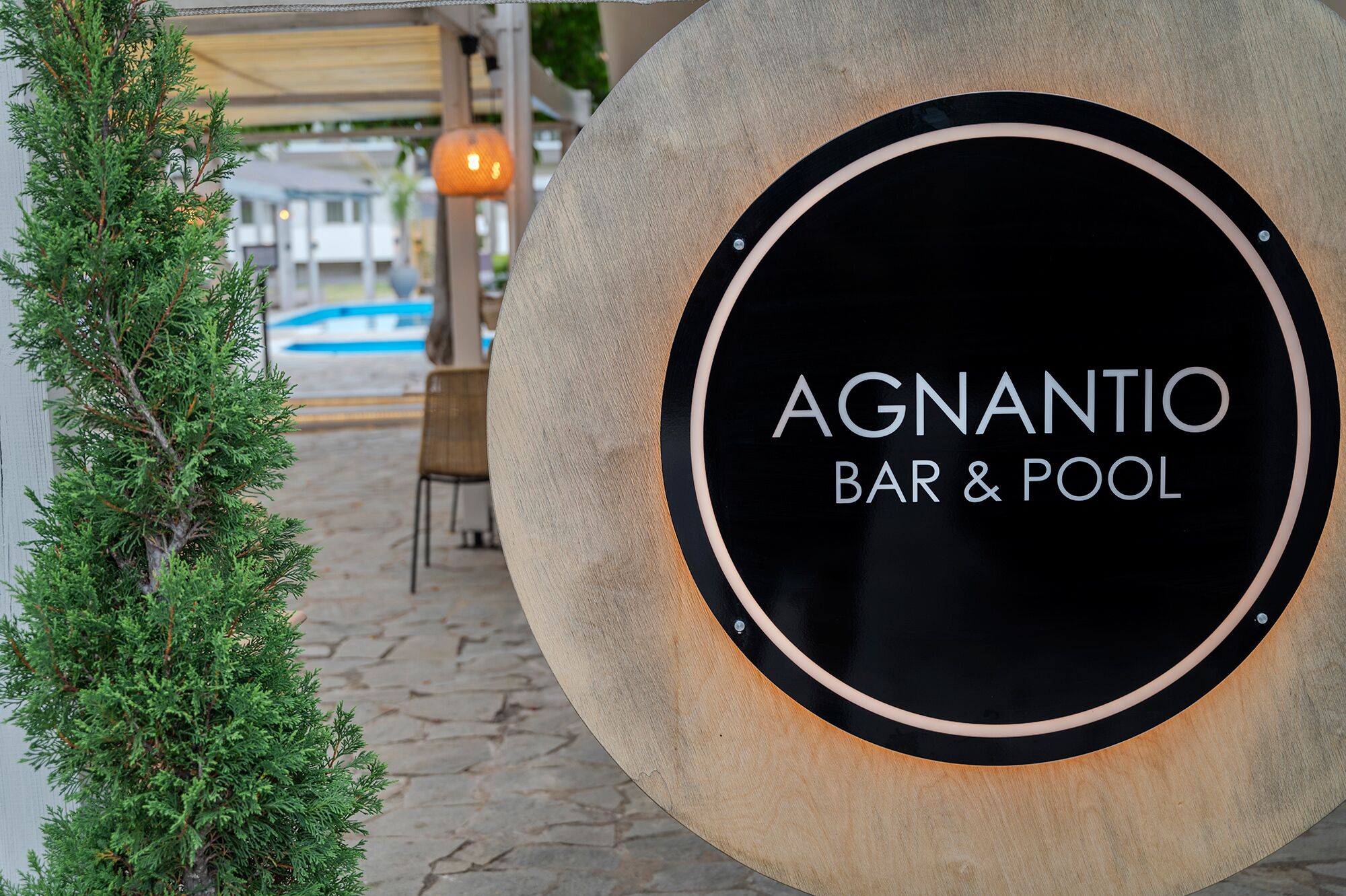 Un letrero para 'AGNANTIO BAR & POOL' con un marco de madera y un fondo circular negro.