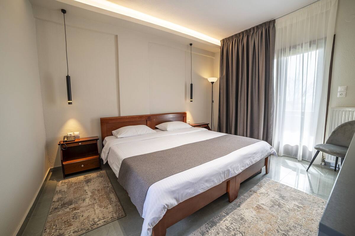 A modern hotel room with a large bed, bedside tables, a desk, and a chair.