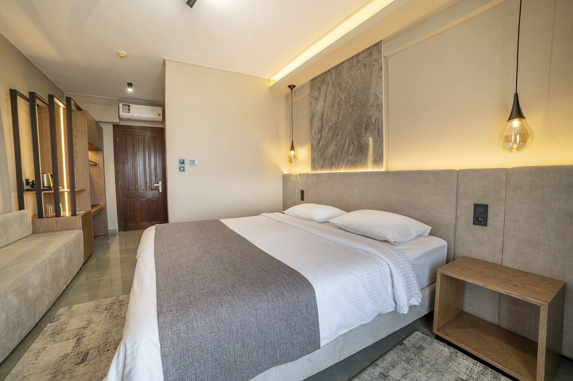 Ett modernt hotellrum med en stor säng, ett sängbord, en soffa och en väggmonterad lampa.