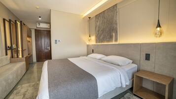 Ett modernt hotellrum med en stor säng, ett sängbord, en soffa och en väggmonterad lampa.