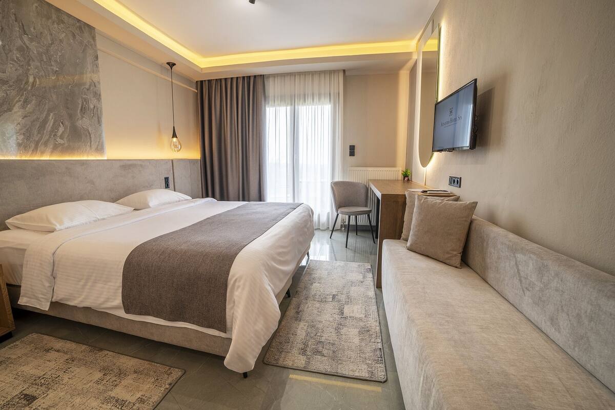 A modern hotel room with a large bed, a sofa, a desk, and a TV.