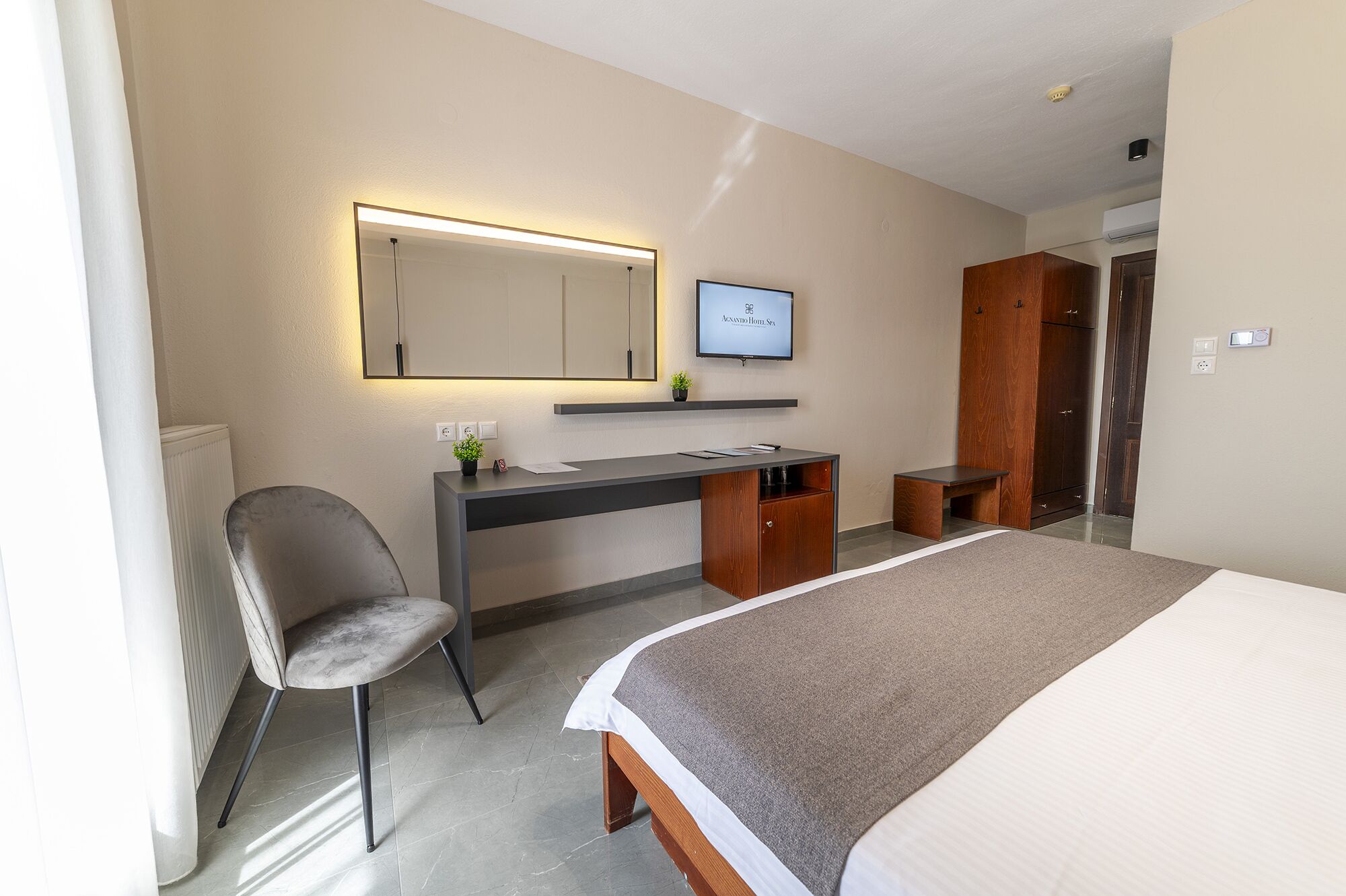 Een hotelkamer met een bed, een bureau met een computer, een stoel, een spiegel en een televisie waarop 'AQUASTUDIO Hotel SPA' staat.