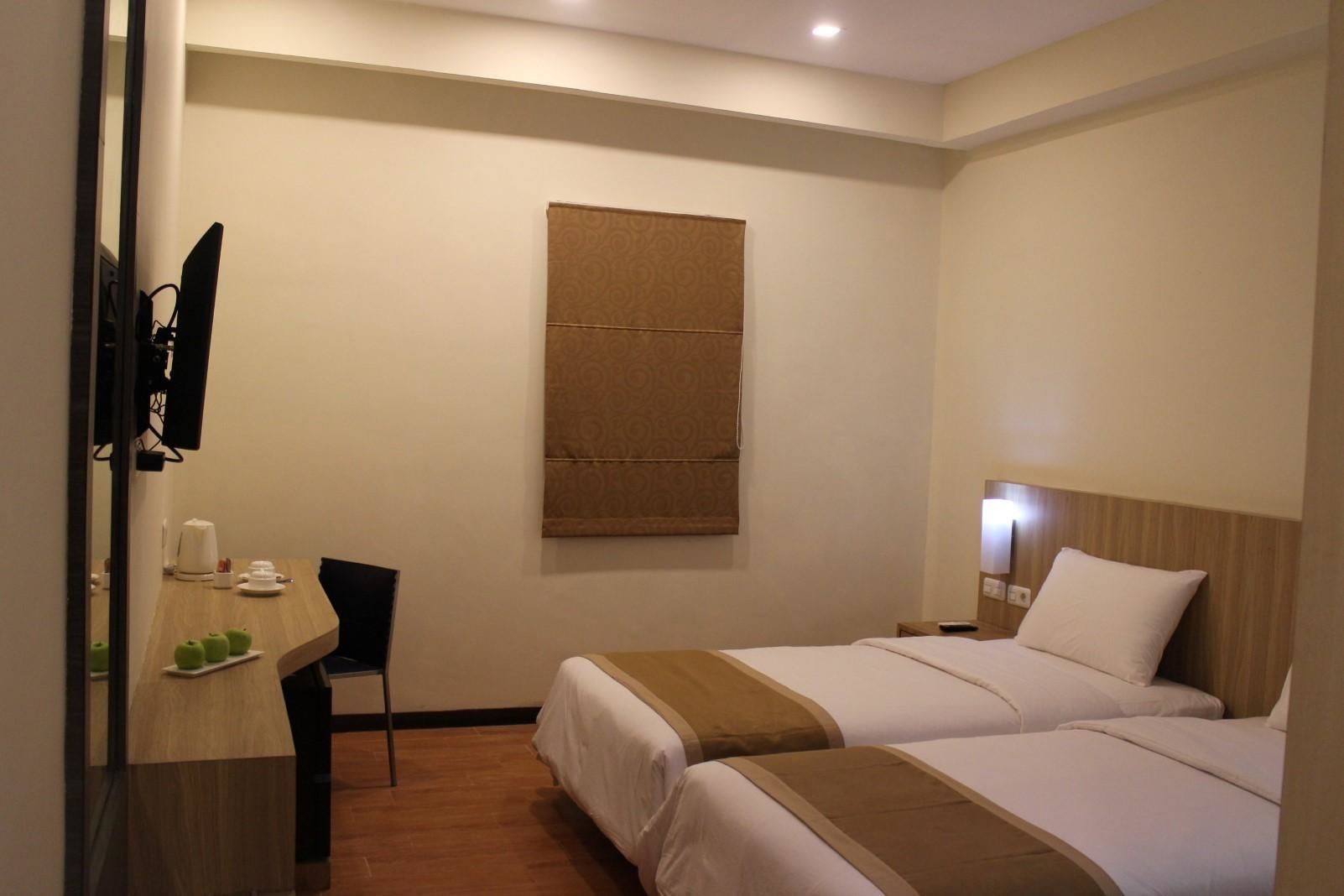 A hotel room with two beds, a desk with a chair, a television, and a large window with a brown curtain.