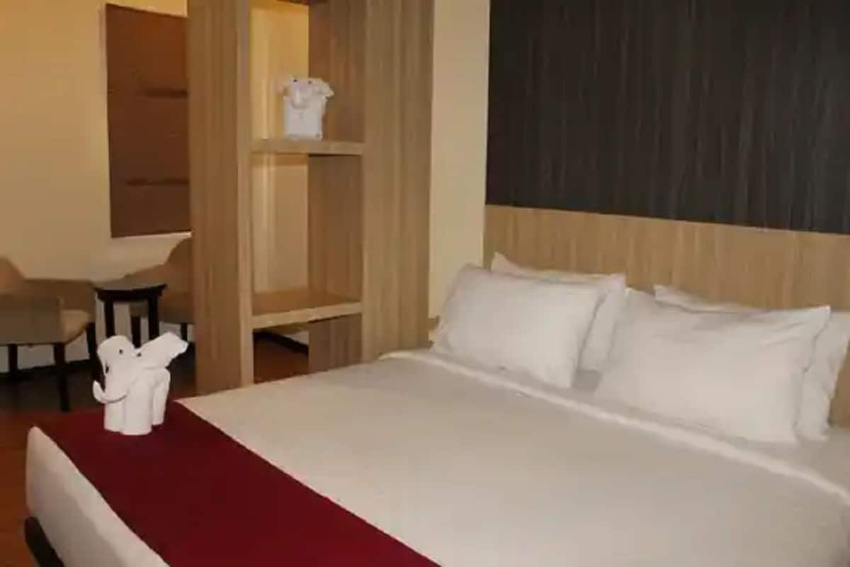Une chambre d’hôtel équipée d’un lit, d’un bureau, d’une chaise et d’une étagère sur laquelle est posé un objet décoratif.