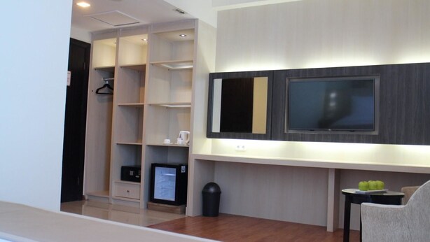 Une chambre d’hôtel moderne avec un plancher en bois, un téléviseur à écran plat fixé au mur, une petite table avec une chaise et un dressing avec des étagères et un four à micro-ondes.
