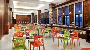 Un vaste espace dédié à la salle à manger, avec de nombreuses tables et chaises, un long comptoir servant de buffet, et de grandes fenêtres ornées de motifs décoratifs.