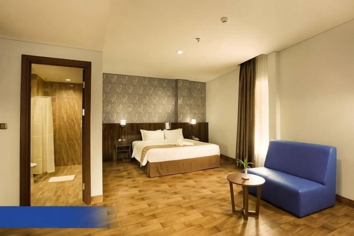 A hotel room with a bed, a blue sofa, a small table, and a mirror.