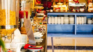 A buffet area with a variety of food containers and utensils, a blue shelving unit with dishes, and a patterned wall. - Horison Express Sentani (Sentani)