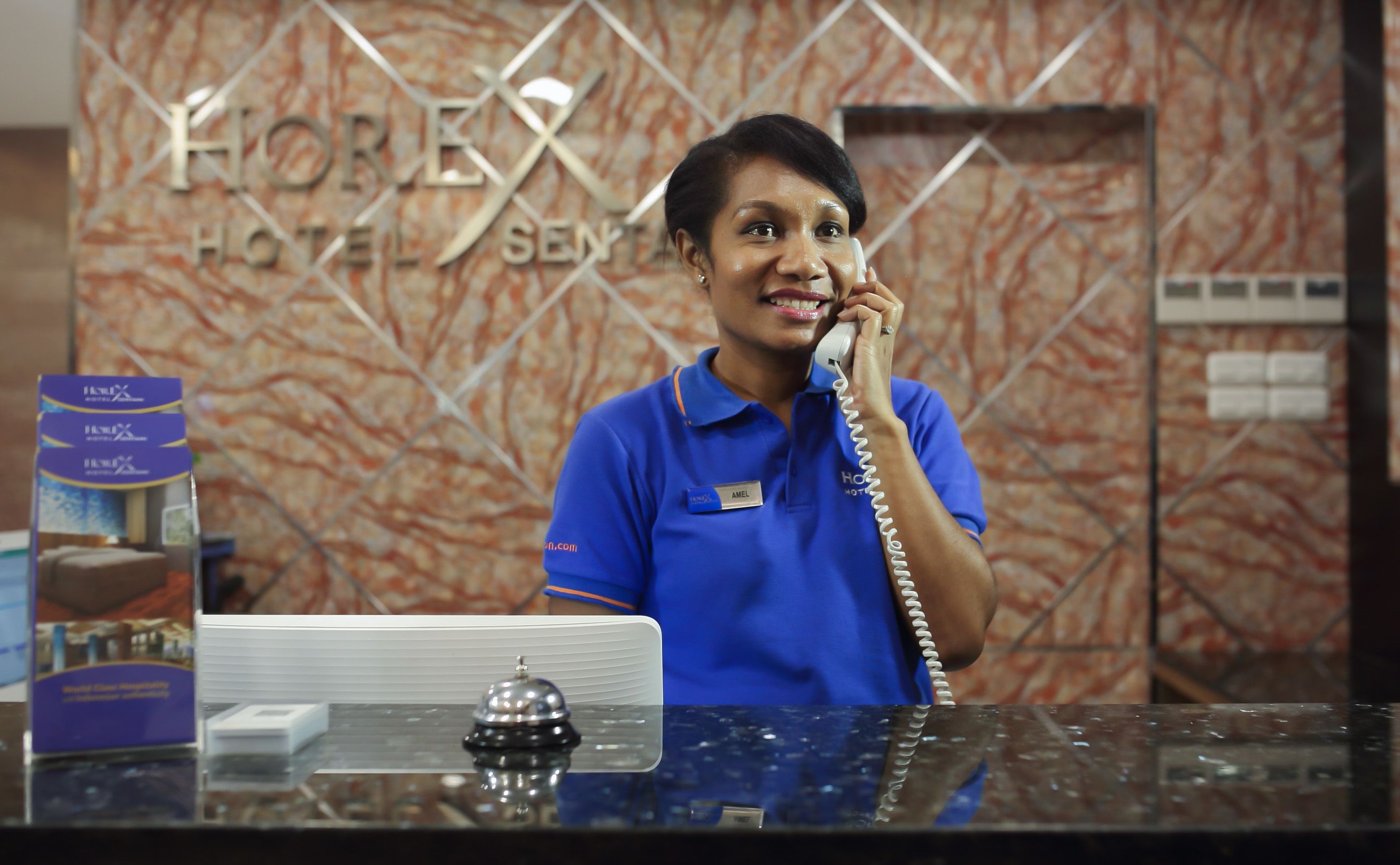 A hotel reception desk with a marble wall background, a name tag, and a hotel sign.