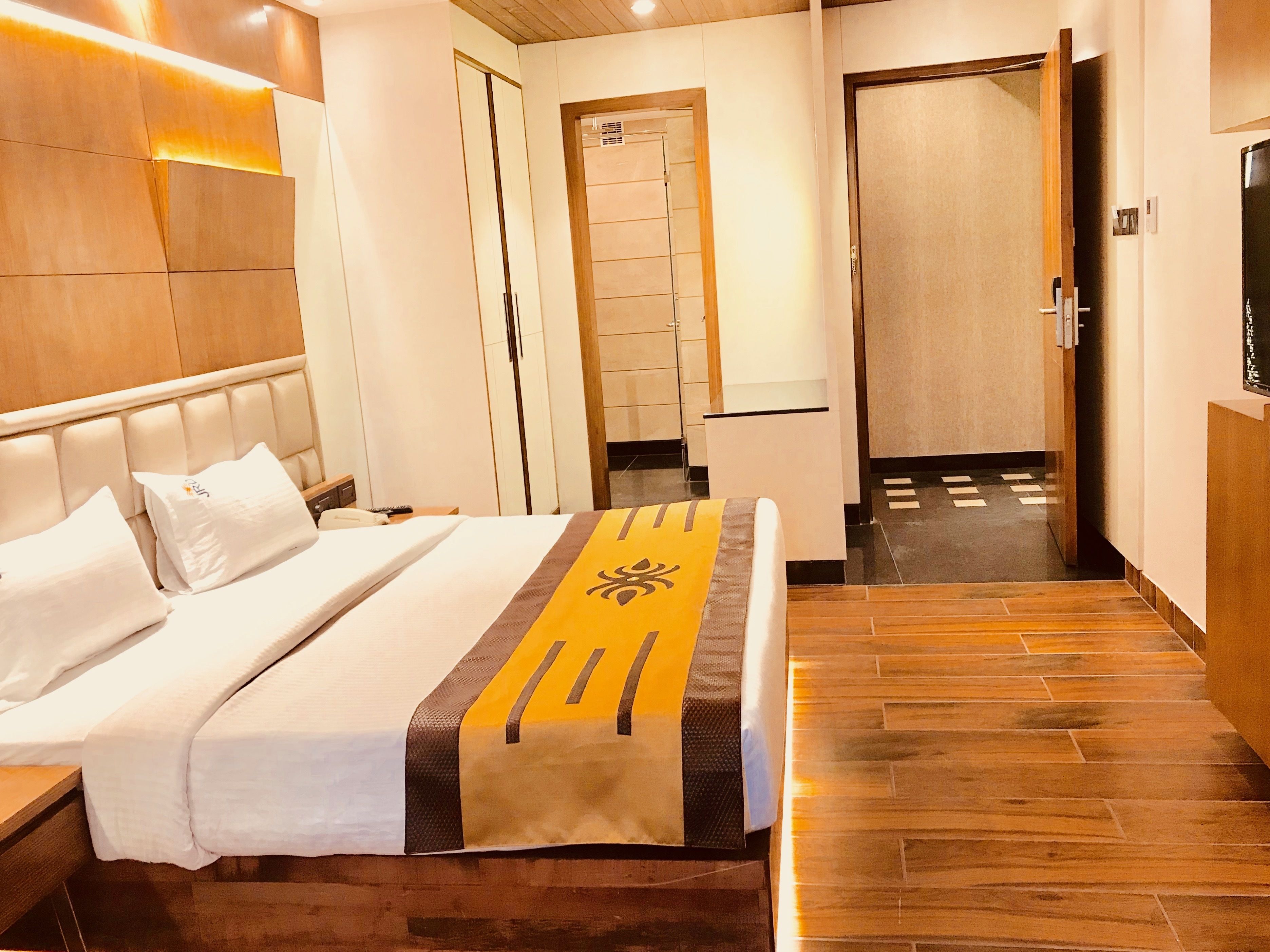 A hotel room with a large bed, a wooden headboard, a wardrobe, and a bathroom visible through an open door.
