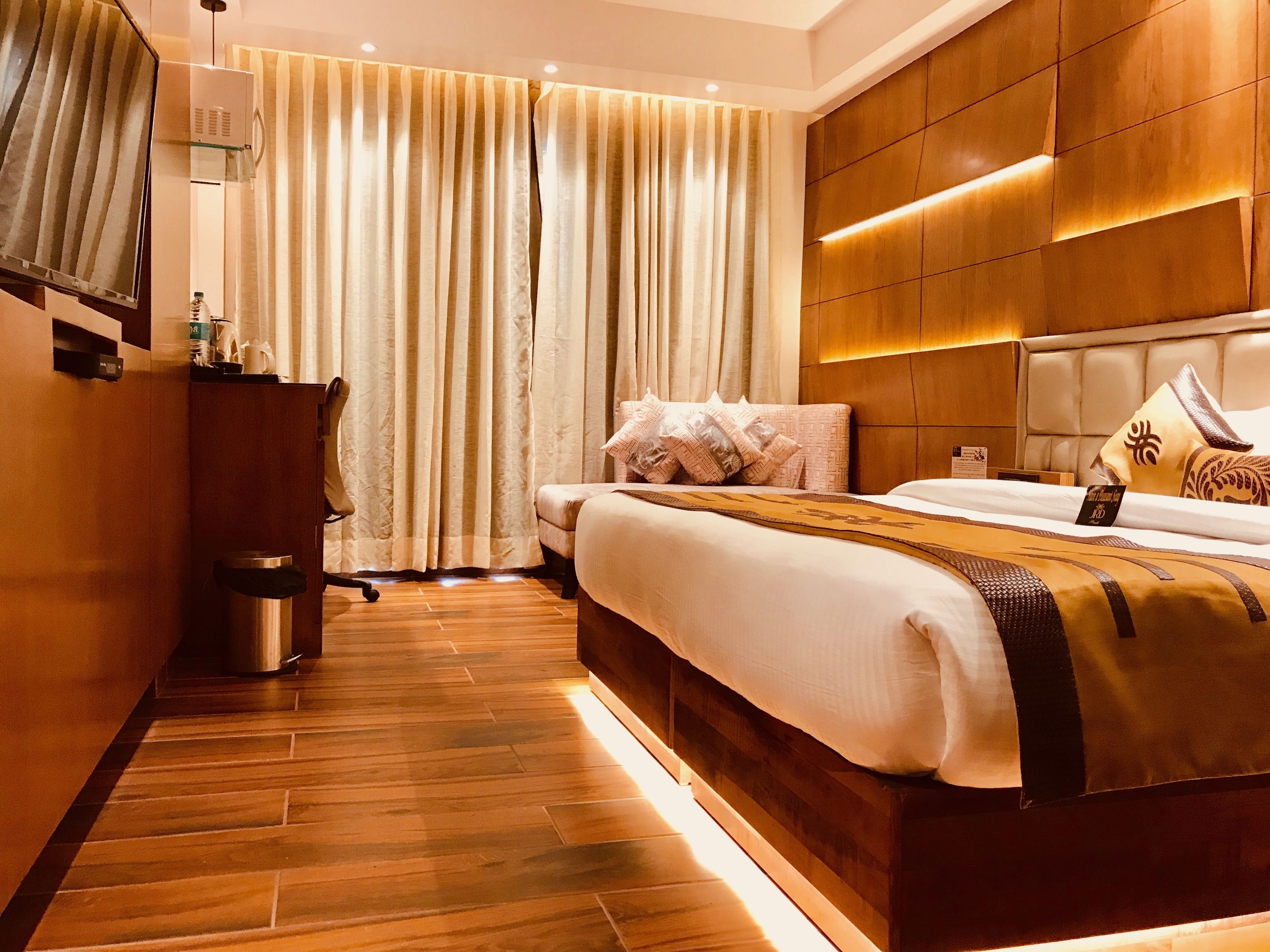 A modern hotel room with a large bed, wooden flooring, a desk with a chair, and a minibar.