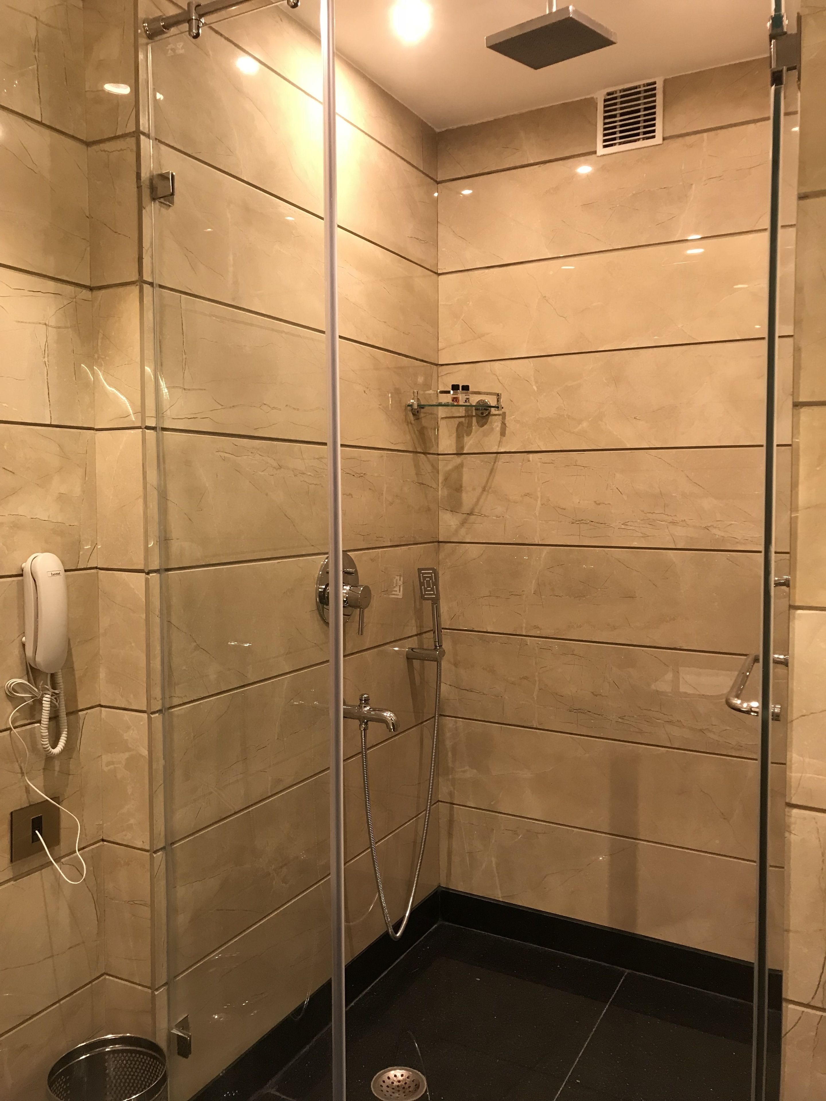 A glass-enclosed shower with a handheld showerhead, a wall-mounted faucet, and a handheld showerhead.