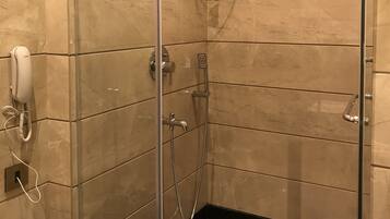 A glass-enclosed shower with a handheld showerhead, a wall-mounted faucet, and a handheld showerhead.