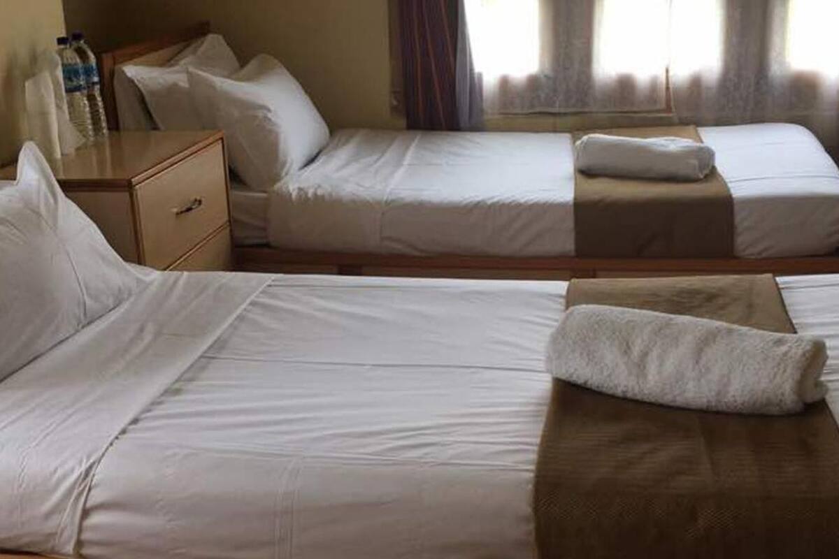 Two single beds with white linens, a wooden nightstand, and a bottle of water on the nightstand.