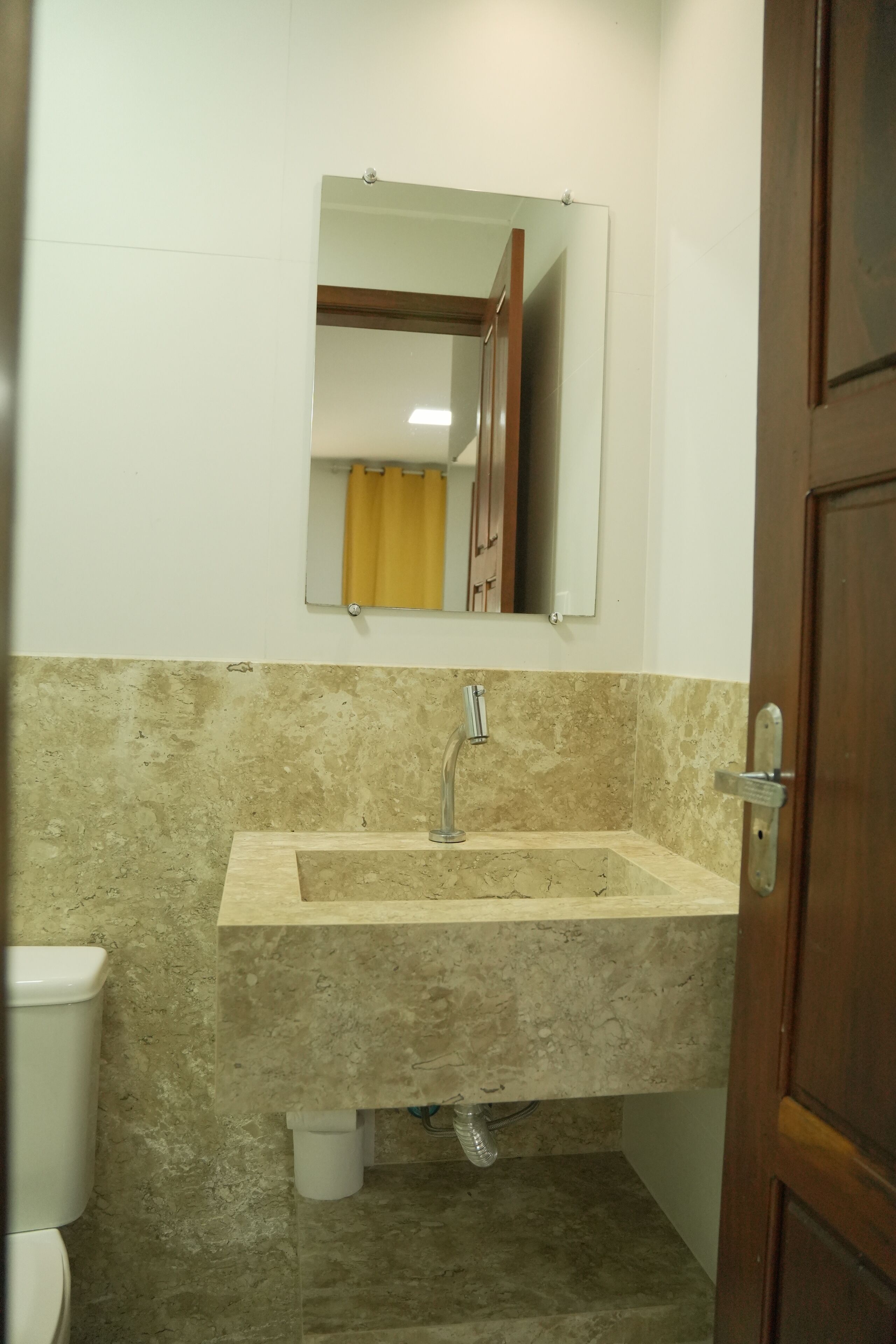 Un baño con lavamanos de mármol, un espejo y una puerta de madera.