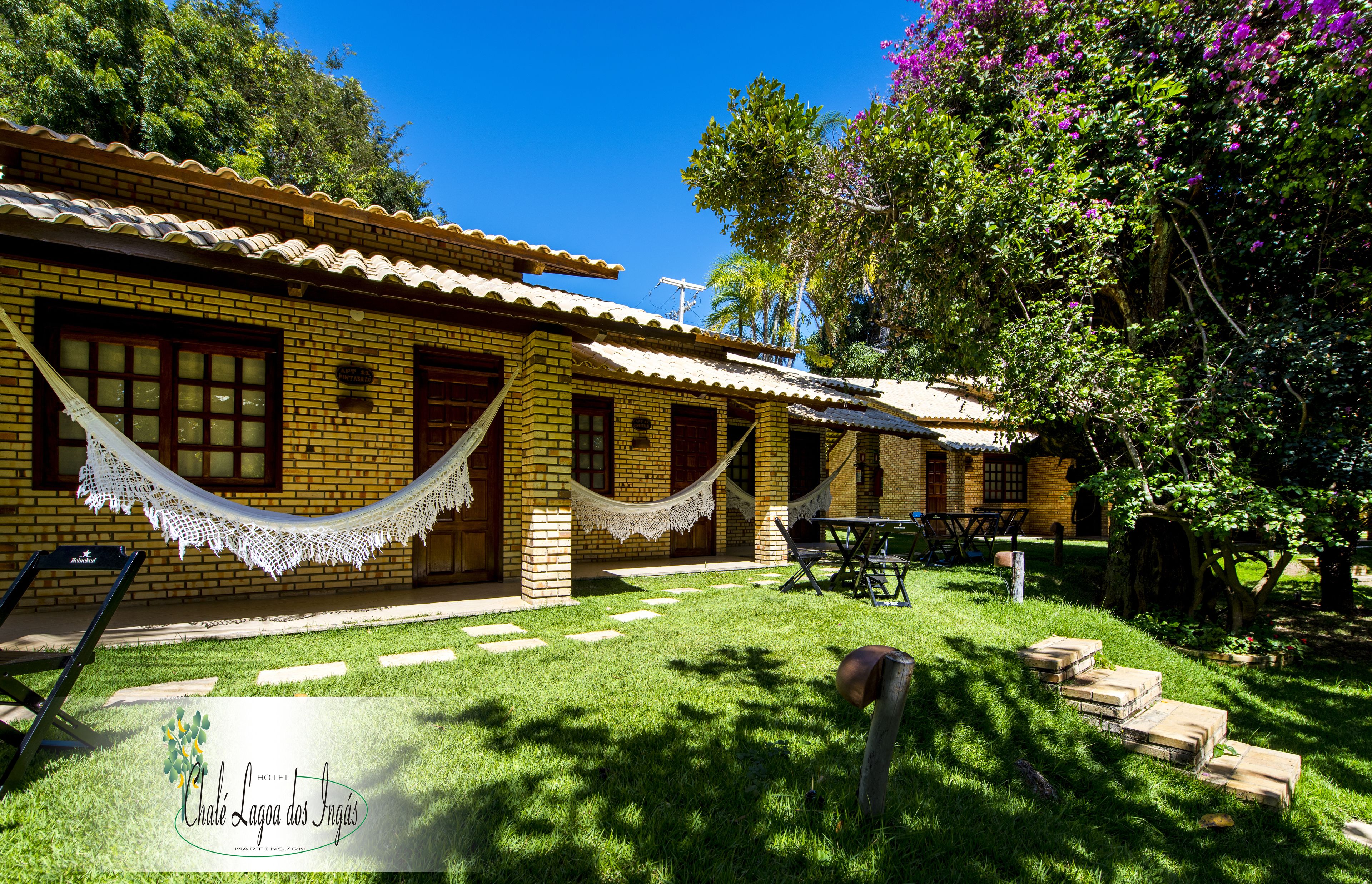 Un hotel con fachada de ladrillo, una hamaca, una mesa de patio y un césped bien cuidado.