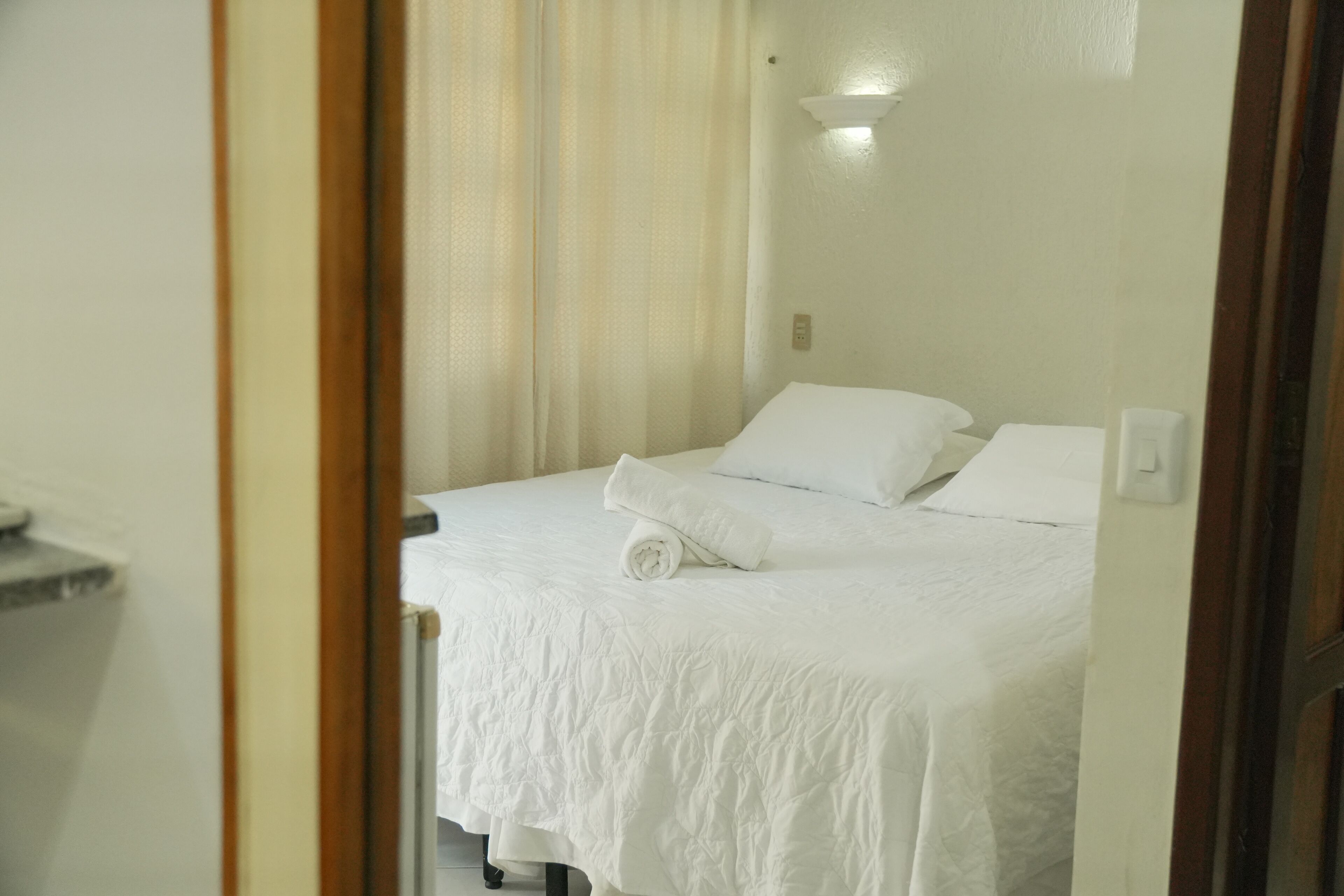 Une chambre d’hôtel avec un lit, une table de chevet et un luminaire fixé au mur.