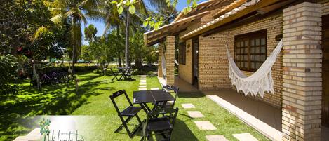 A patio area with a table and chairs, a hammock, and a brick building with a tiled roof.