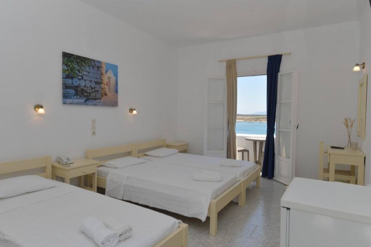 Una stanza con tre letti singoli, una scrivania, una sedia e un tavolino. Al muro è presente un quadro e si gode di vista mare attraverso una porta aperta.