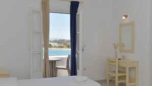 A hotel room with a bed, a desk, a chair, and a view of the sea. - Bocamviglies By The Sea (Paros)