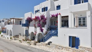 A white building with blue shutters and balconies, stone steps, and a clear sky. - Bocamviglies By The Sea (Paros)