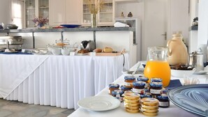 A breakfast buffet setup with various food items and a pitcher of orange juice. - Bocamviglies By The Sea (Paros)
