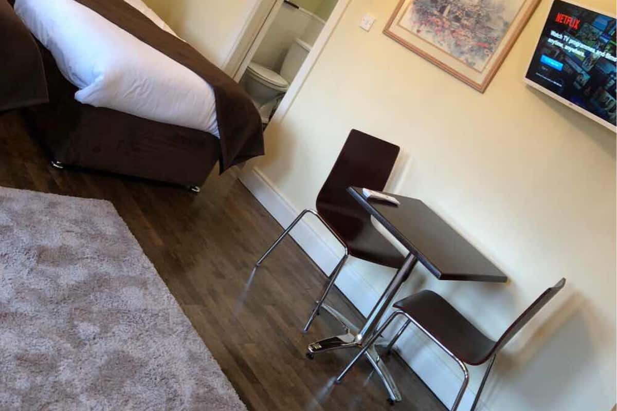 Hotellihuone, jossa on parivuode, työpöytä tuolilla, pieni pöytä ja seinällä kehystetty kuva.