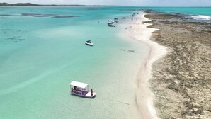 An aerial view of a beach with clear turquoise waters, a sandy shore, and several boats.