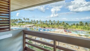 A balcony with a view of a resort pool area, palm trees, and the ocean.