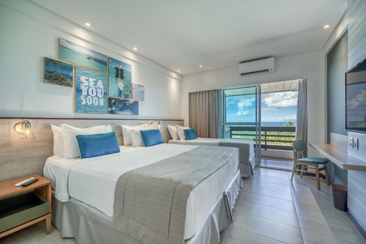 Une chambre d’hôtel avec deux lits, un bureau, une chaise, une télévision et un balcon avec vue.